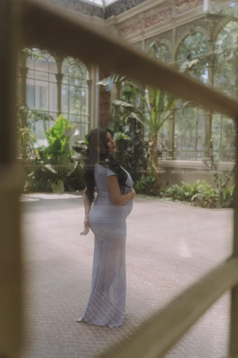 Elegant pregnant woman in a lavender dress poses peacefully in a sunlit conservatory, Vacation Portraits photoshoot.