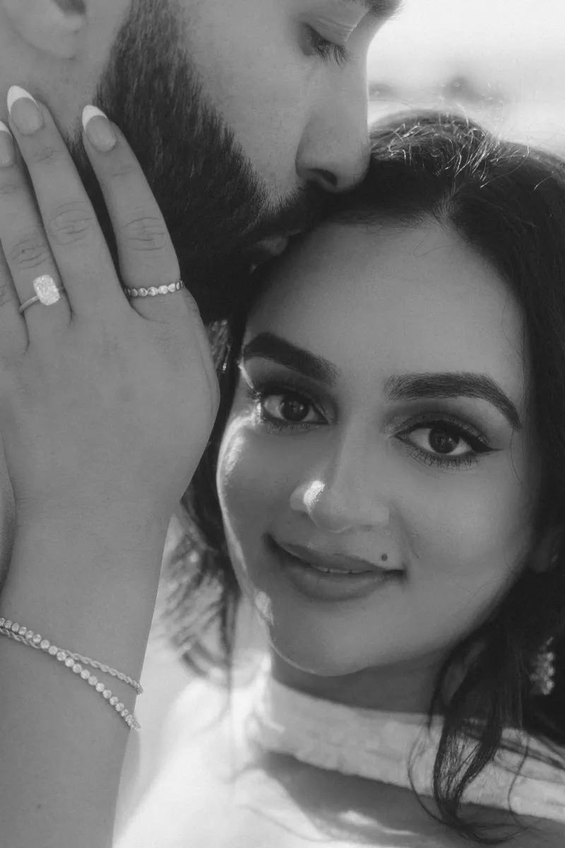 Emotional moment during a surprise proposal photoshoot, bride-to-be smiles as fiancé kisses her forehead.