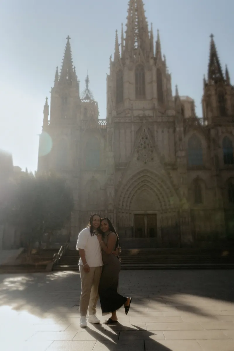 Engaged couple embraces and smiles in soft morning light outside Barcelona Cathedral during a surprise proposal shoot.