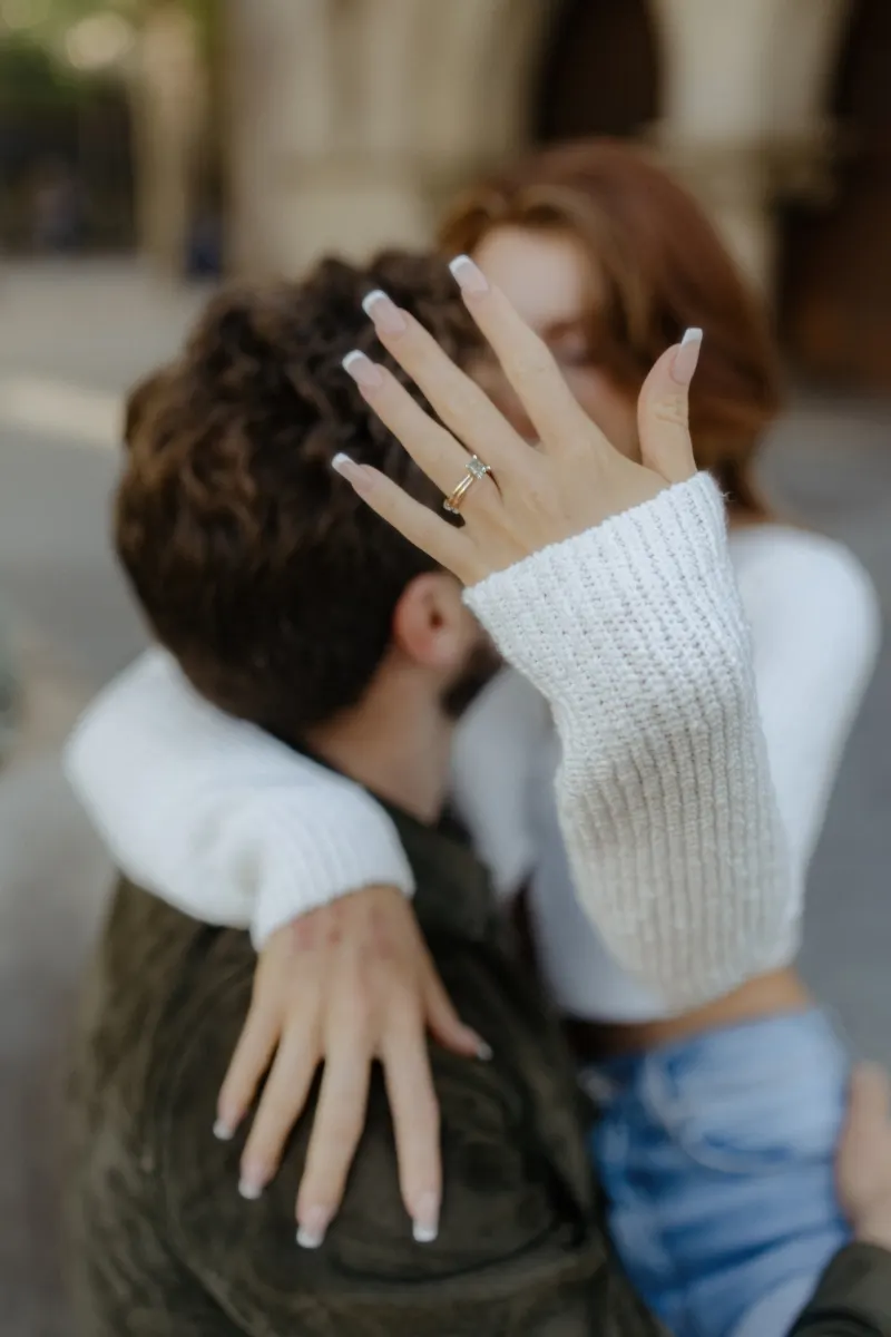 Engaged couple embraces outdoors as she shows off her ring, captured during a couples & engagements photoshoot.