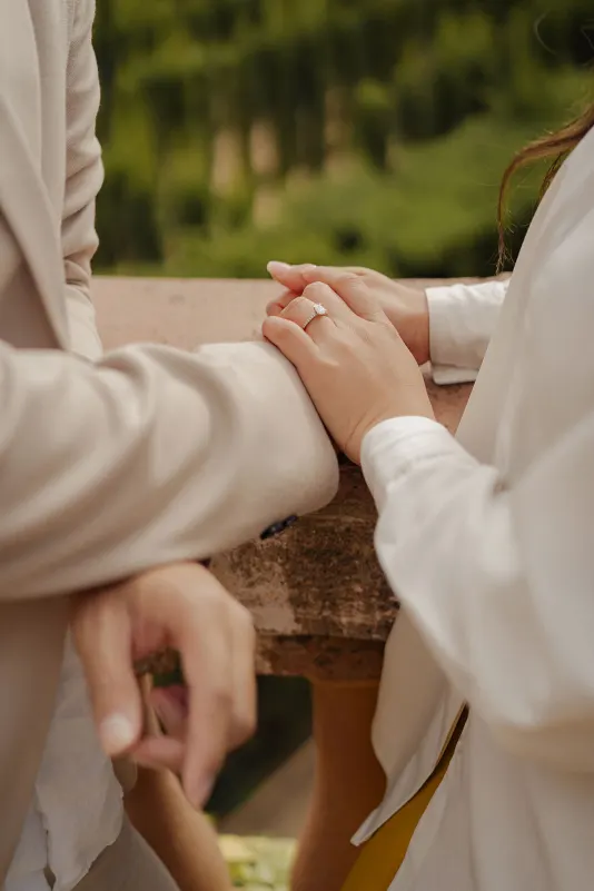Engaged couple gently holding hands on a stone terrace, showcasing the ring during a couples & engagements photoshoot.
