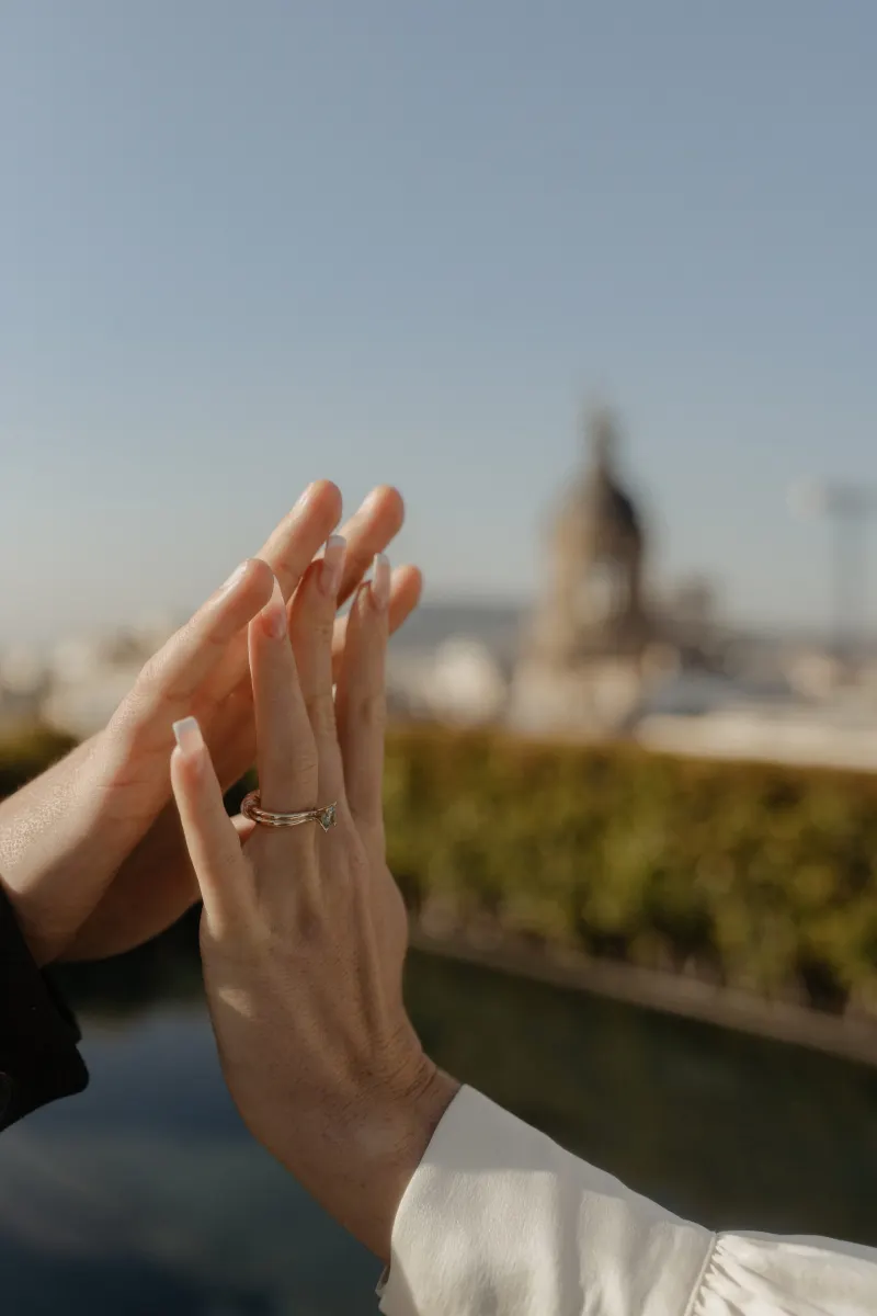 Engaged couple gently touch hands, showing off an engagement ring during a rooftop couples photoshoot.