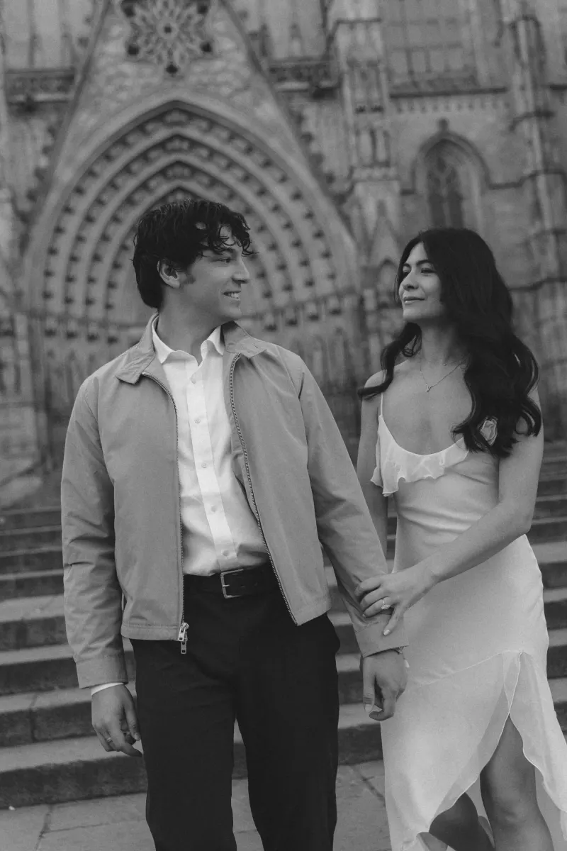 Engaged couple holding hands and smiling at each other on cathedral steps during a couples & engagements photoshoot.