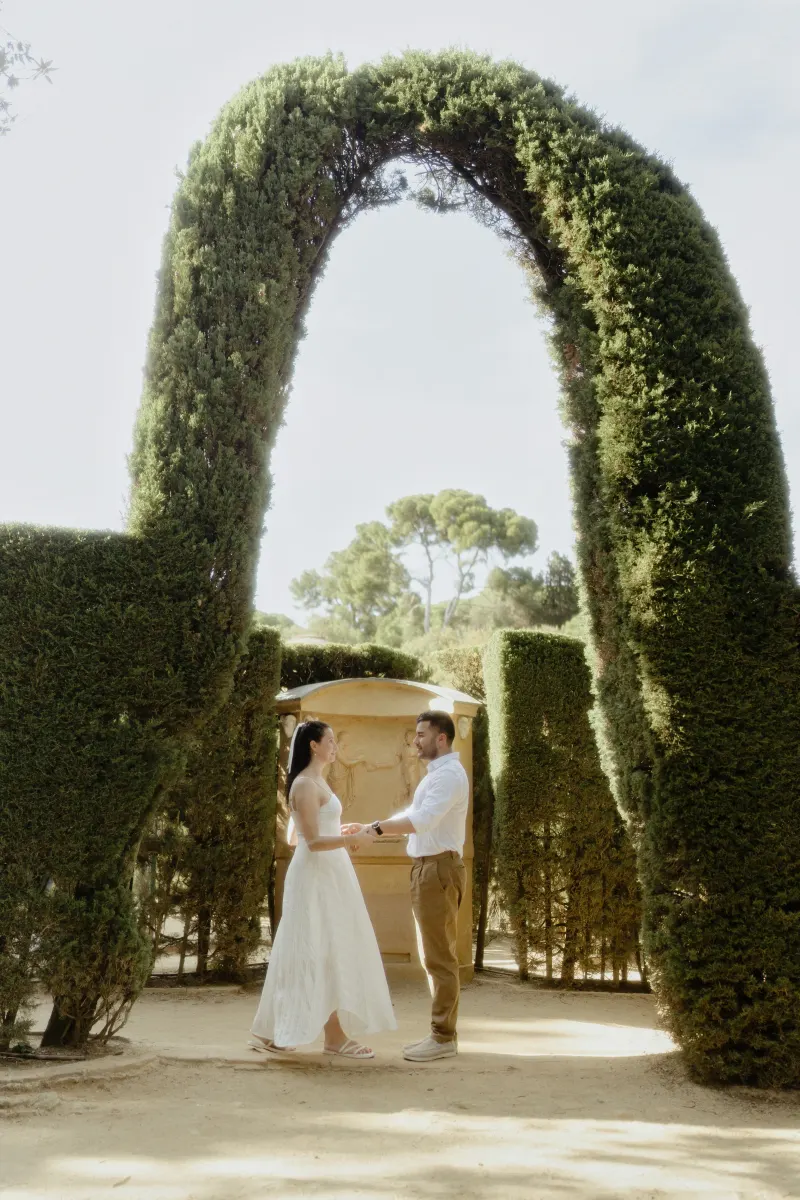 Engaged couple holding hands and smiling under a lush garden arch, captured during a couples photoshoot.