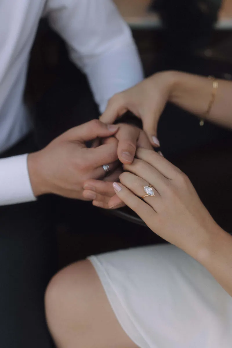 Engaged couple holding hands, her diamond ring sparkling, capturing a tender moment during a couples & engagements photoshoot