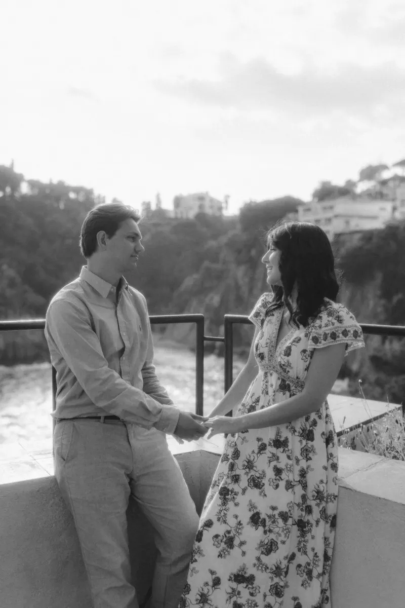 Engaged couple holds hands and smiles at each other on a Mediterranean terrace during a surprise proposal photoshoot.