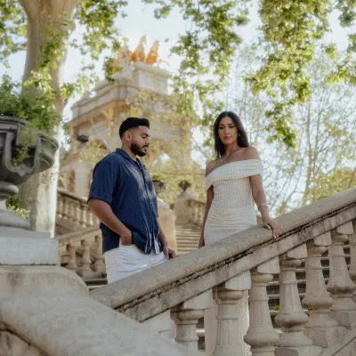 Engaged couple poses on elegant stone stairs in a sunlit park, captured during a couples photoshoot in Barcelona.