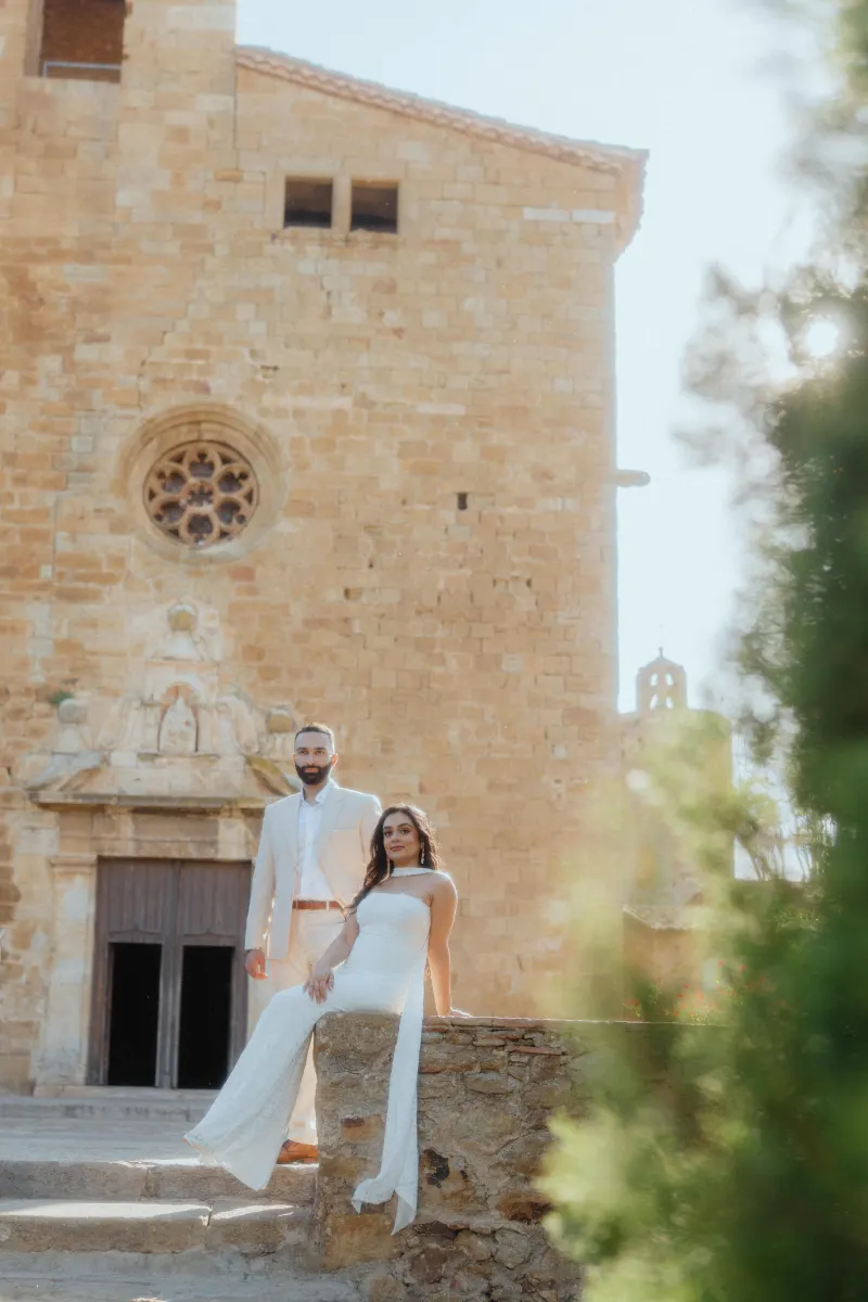 Engaged couple poses on sunlit stone steps in front of a historic church during their surprise proposal photoshoot.