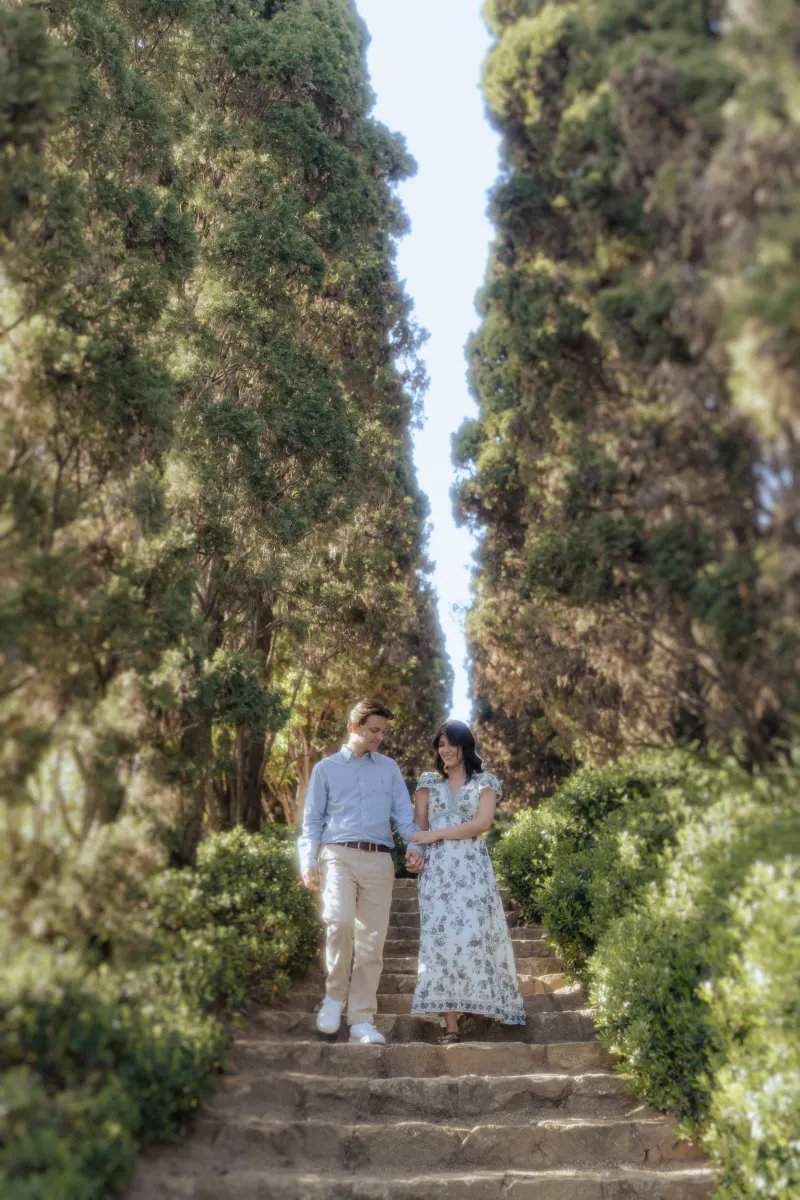 Engaged couple shares a joyful moment walking down garden steps, captured during a surprise proposal photoshoot.