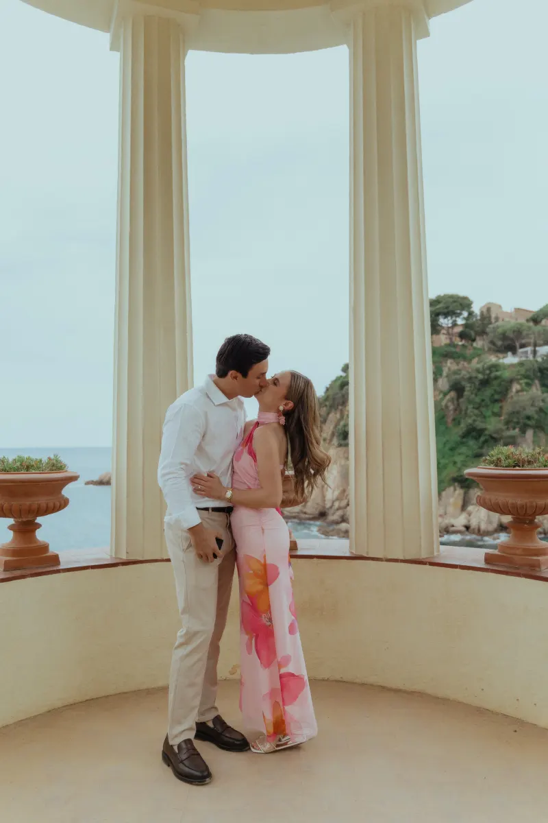 Engaged couple shares a romantic kiss in a seaside pavilion after a surprise proposal photoshoot.