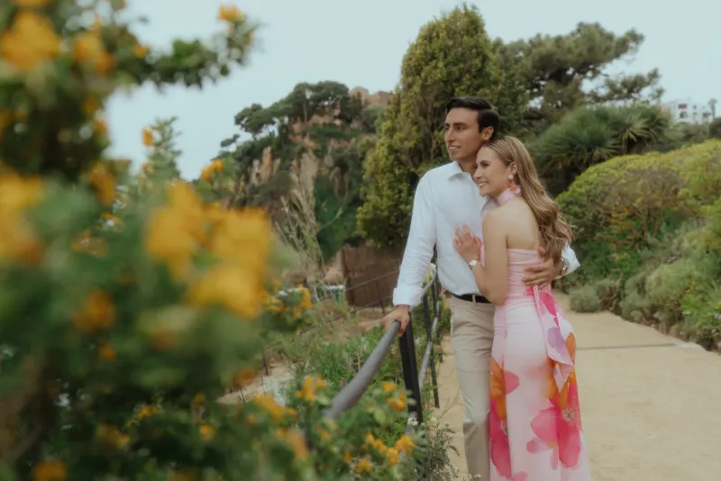 Engaged couple shares a tender embrace on a scenic garden path during a surprise proposal photoshoot by the coast.
