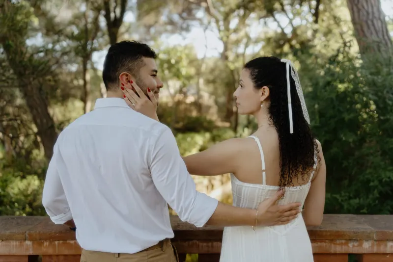 Engaged couple shares a tender moment on a garden terrace, her hand gently resting on his cheek during their photoshoot.