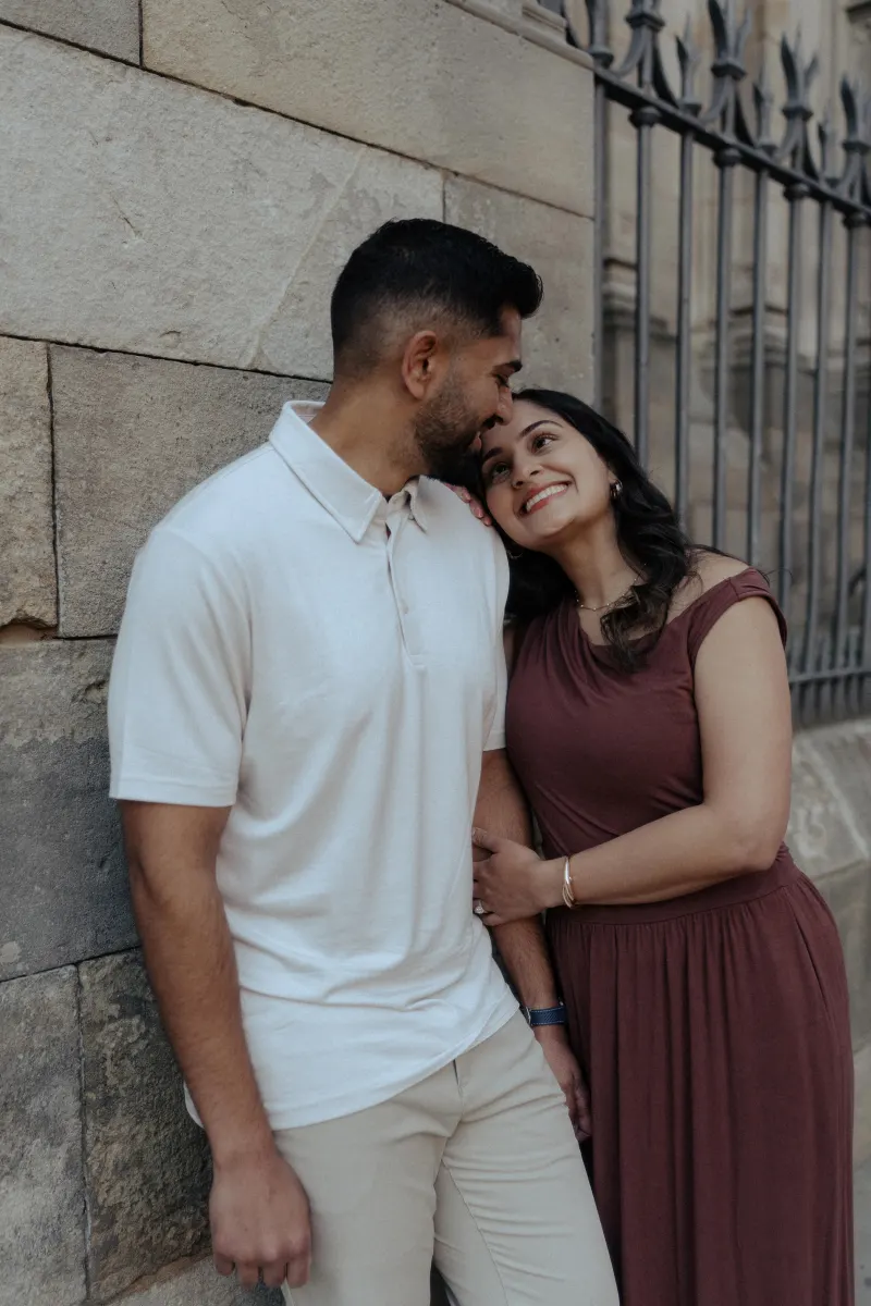 Engaged couple sharing a joyful moment, leaning close together during a couples photoshoot by a stone wall.