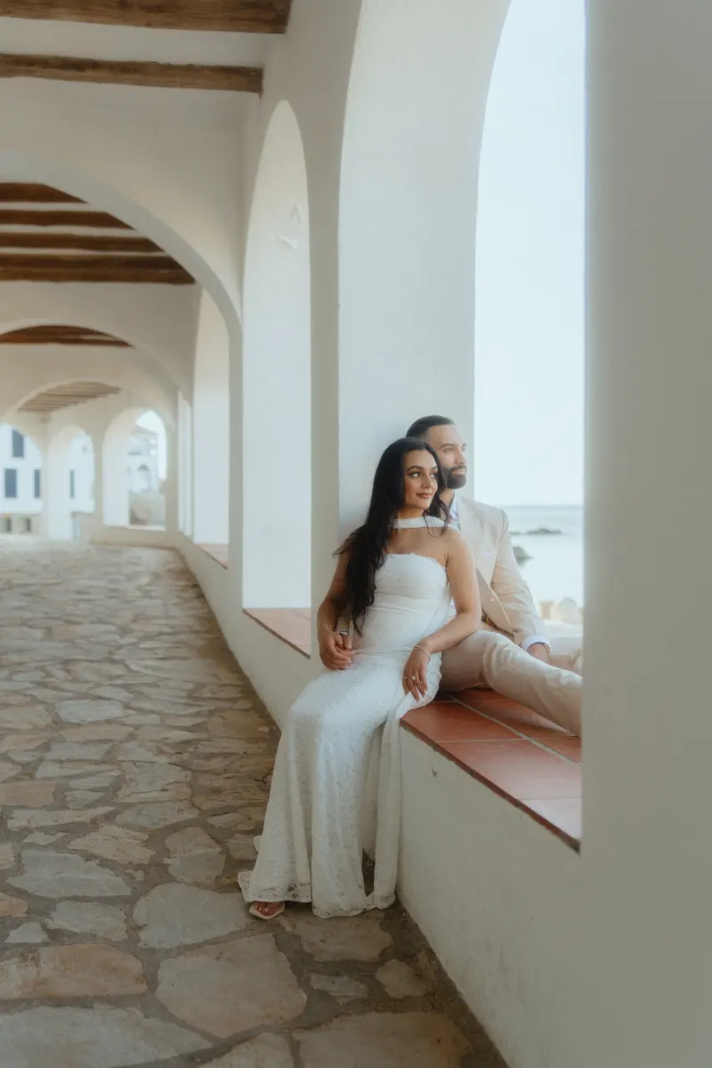 Engaged couple sits together in a sunlit corridor by the sea, captured during a surprise proposal photoshoot.