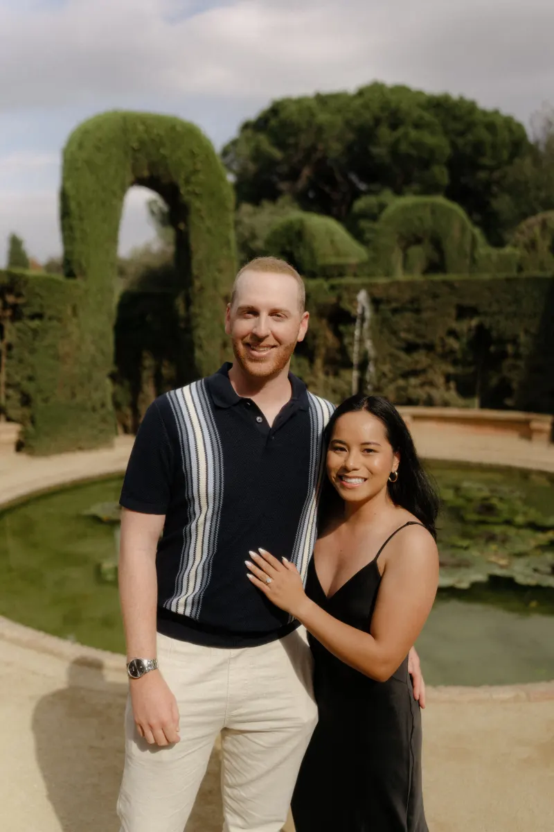 Engaged couple smiles by a garden pond, celebrating their surprise proposal during a professional photoshoot.