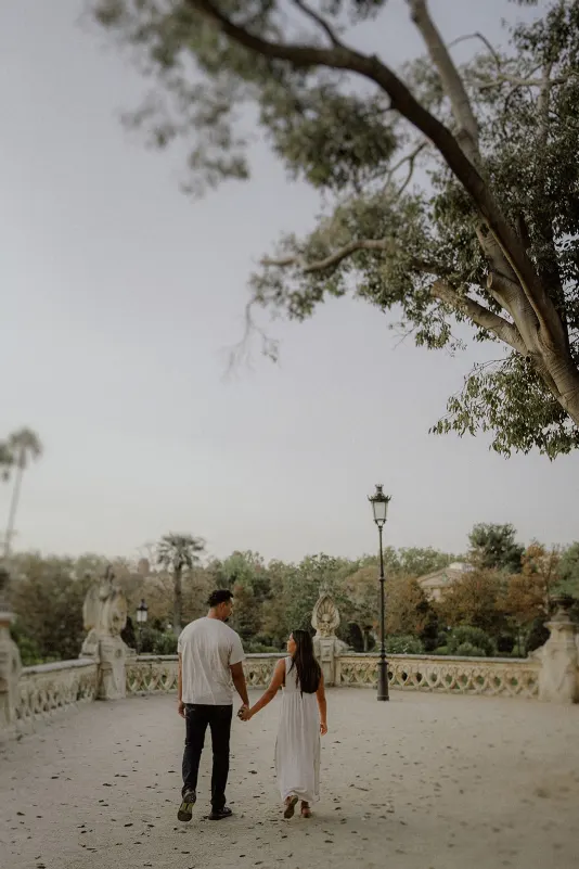 Engaged couple walking hand in hand along a tree-lined terrace, sharing a quiet moment during their photoshoot session.