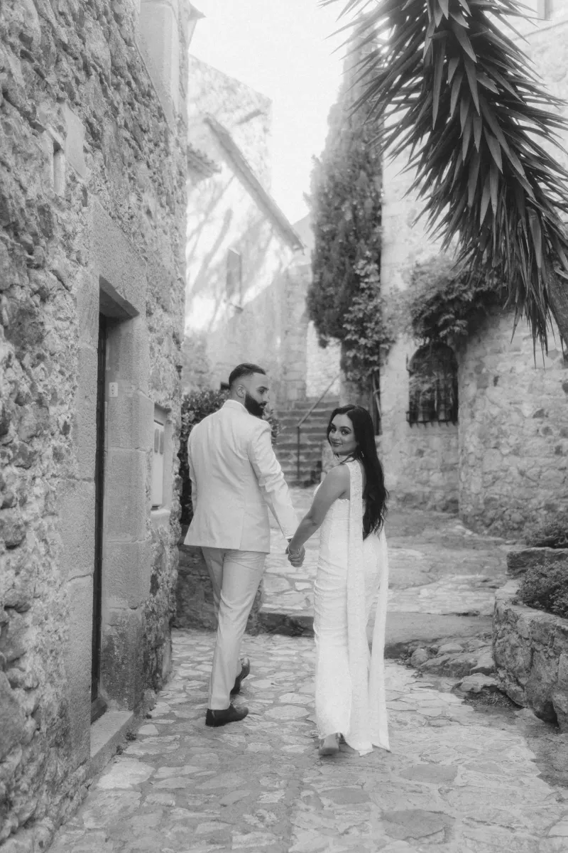 Engaged couple walks hand in hand through a rustic stone alley, smiling after their surprise proposal photoshoot.