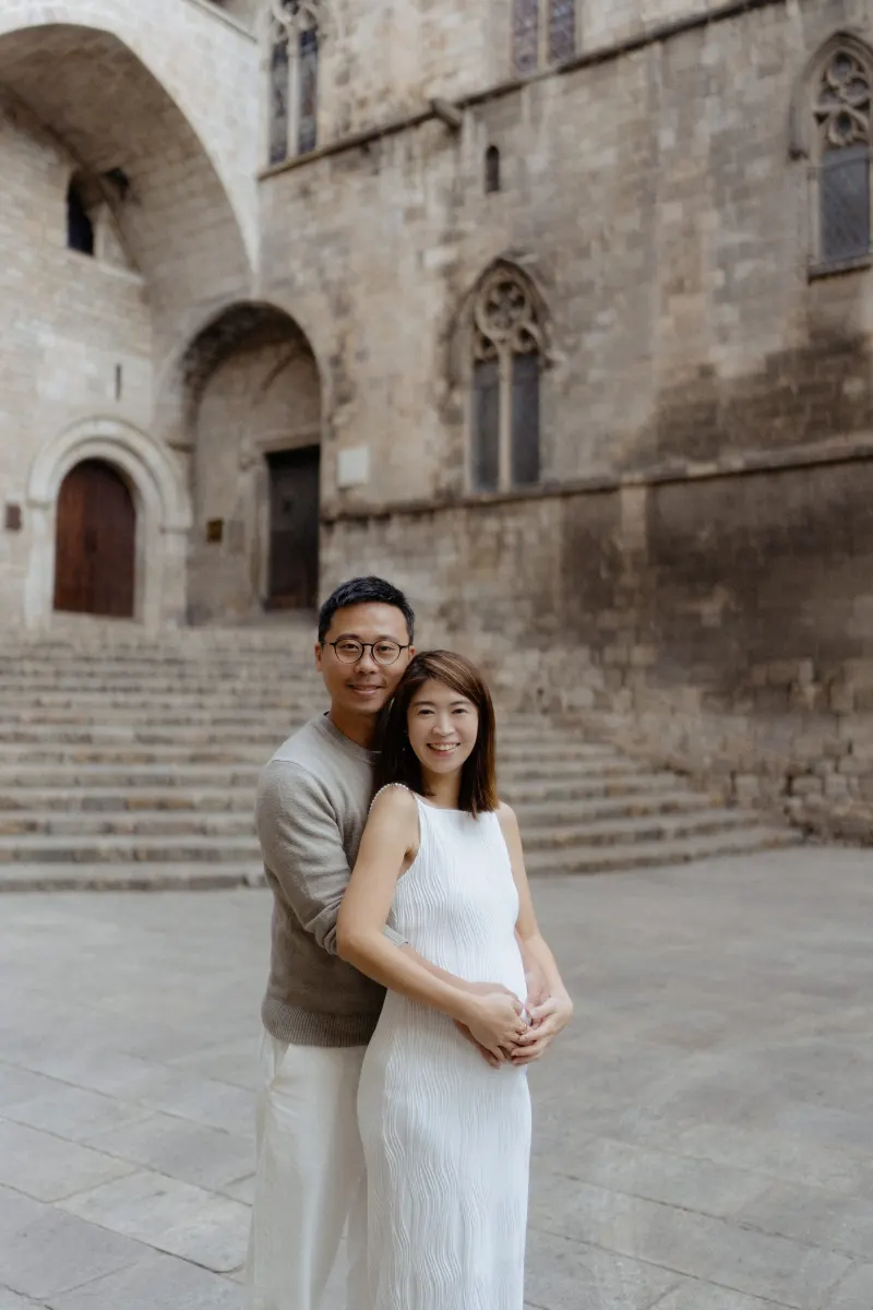 Expectant couple embraces and smiles during a Vacation Portraits photoshoot in Barcelona’s historic Gothic Quarter.
