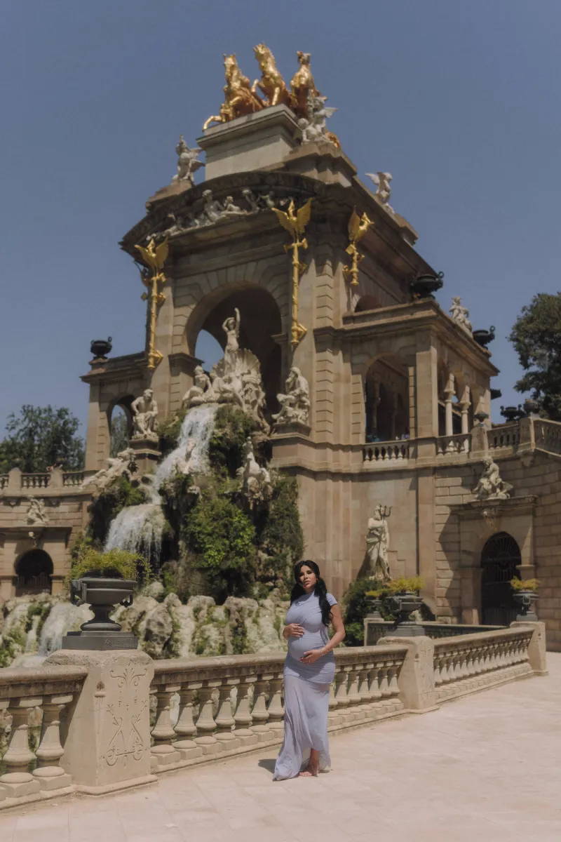 Expectant mother in a soft blue dress poses by the grand fountain at Parc de la Ciutadella, Vacation Portraits session.