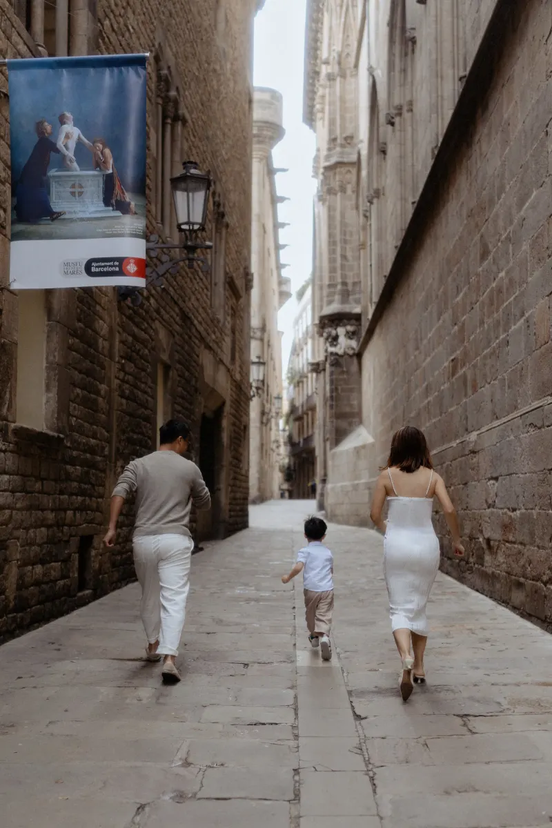 Family joyfully walking hand in hand down a historic Barcelona alley during a Vacation Portraits photoshoot.