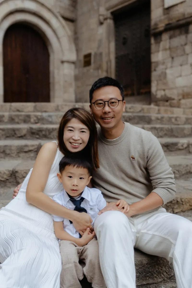 Family sits close together on stone steps, smiling during a Vacation Portraits photoshoot in historic Barcelona.