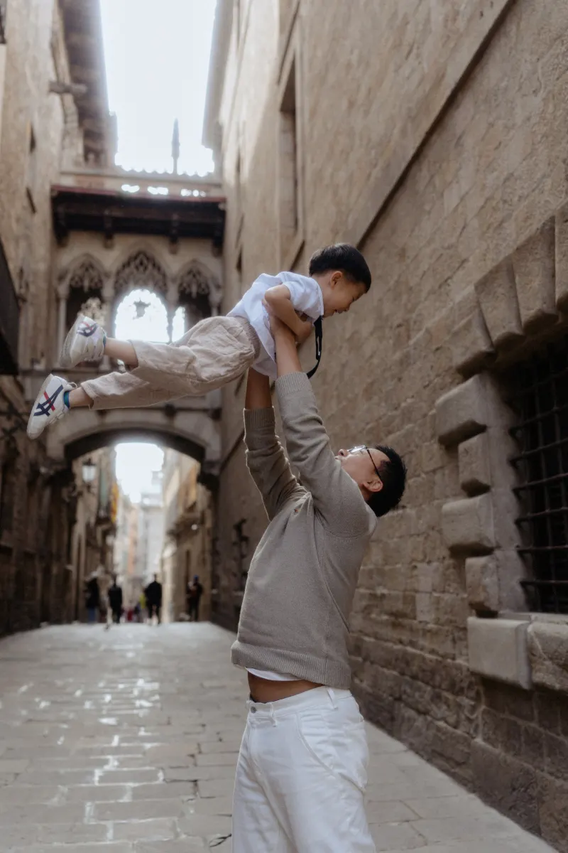 Father lifts his laughing son in the air during a Vacation Portraits photoshoot in Barcelona’s Gothic Quarter.