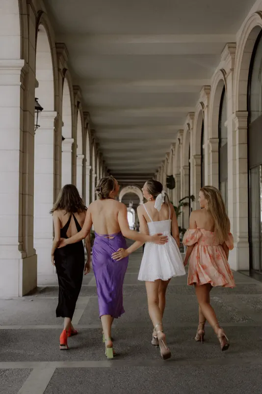 Four friends in colorful dresses walk arm in arm under elegant arches, Vacation Portraits photoshoot in the city.