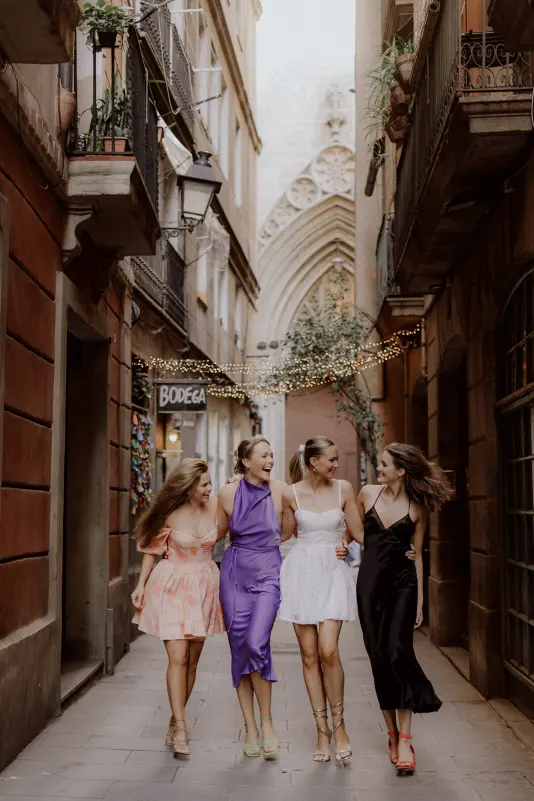 Four women in colorful dresses walk arm in arm, laughing together on a charming Barcelona street, Vacation Portraits session.