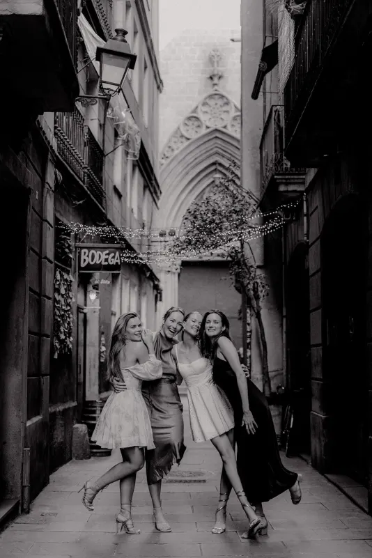 Four women in elegant dresses laugh together in a charming European alley, Vacation Portraits photoshoot capturing friendship