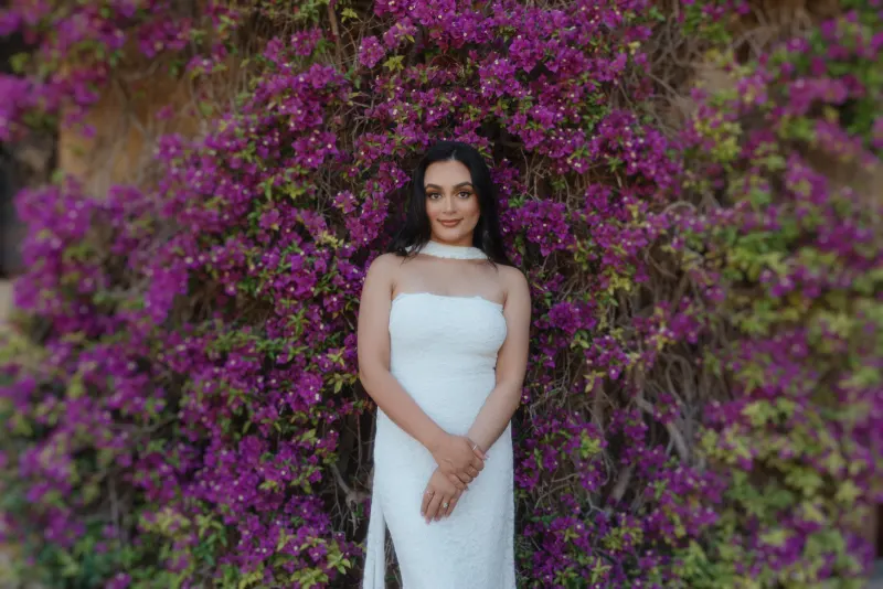 Future bride in a white dress stands before blooming bougainvillea, captured during a surprise proposal photoshoot.