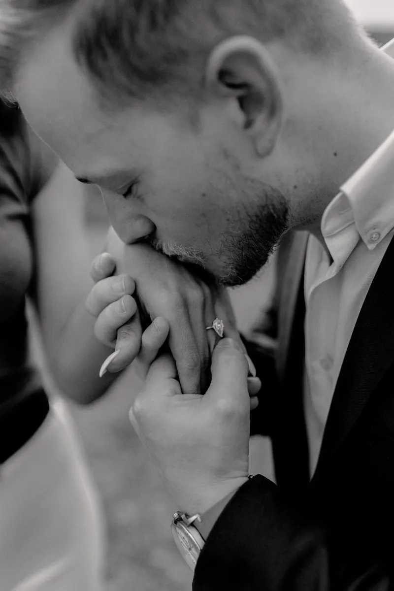 Groom-to-be kisses fiancée’s hand, highlighting her engagement ring during a countryside surprise proposal photoshoot.
