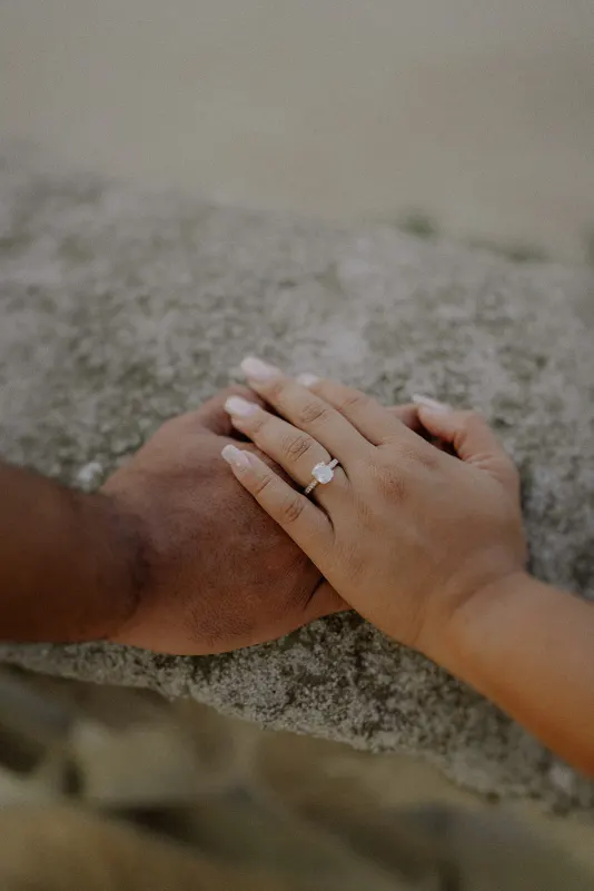 Hands gently intertwined on a stone ledge, highlighting an engagement ring during a couples photoshoot session.