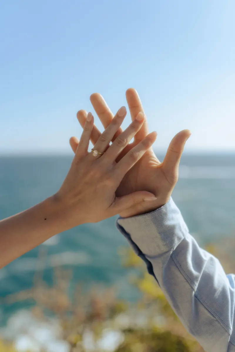 Hands intertwined, engagement ring sparkling, captured during a surprise proposal photoshoot by the ocean.