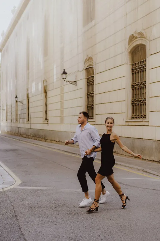 Happy couple holding hands and crossing a quiet city street, captured during a couples & engagements photoshoot session.