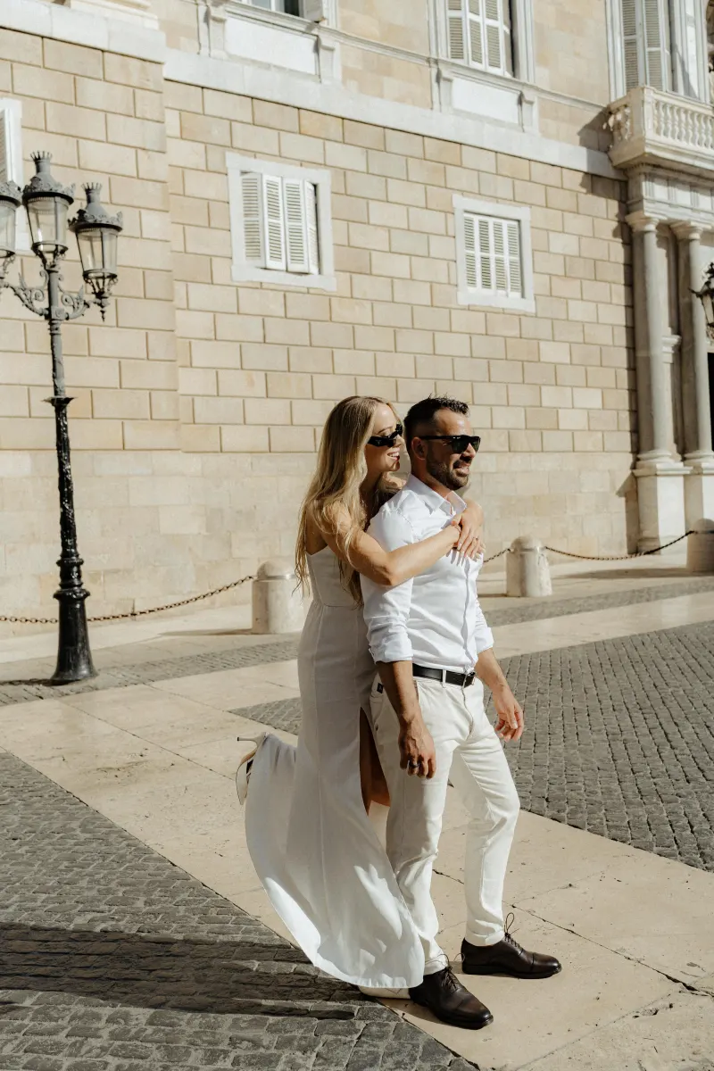 Happy couple in coordinated white outfits share a playful embrace during a couples & engagements shoot on a sunny city street
