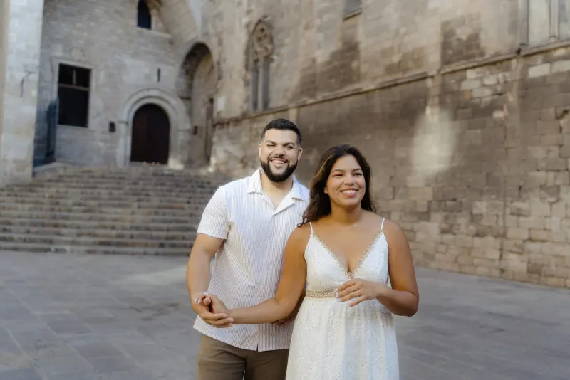 Happy couple walks hand in hand, smiling and relaxed, during a couples & engagements photoshoot in a historic city square.