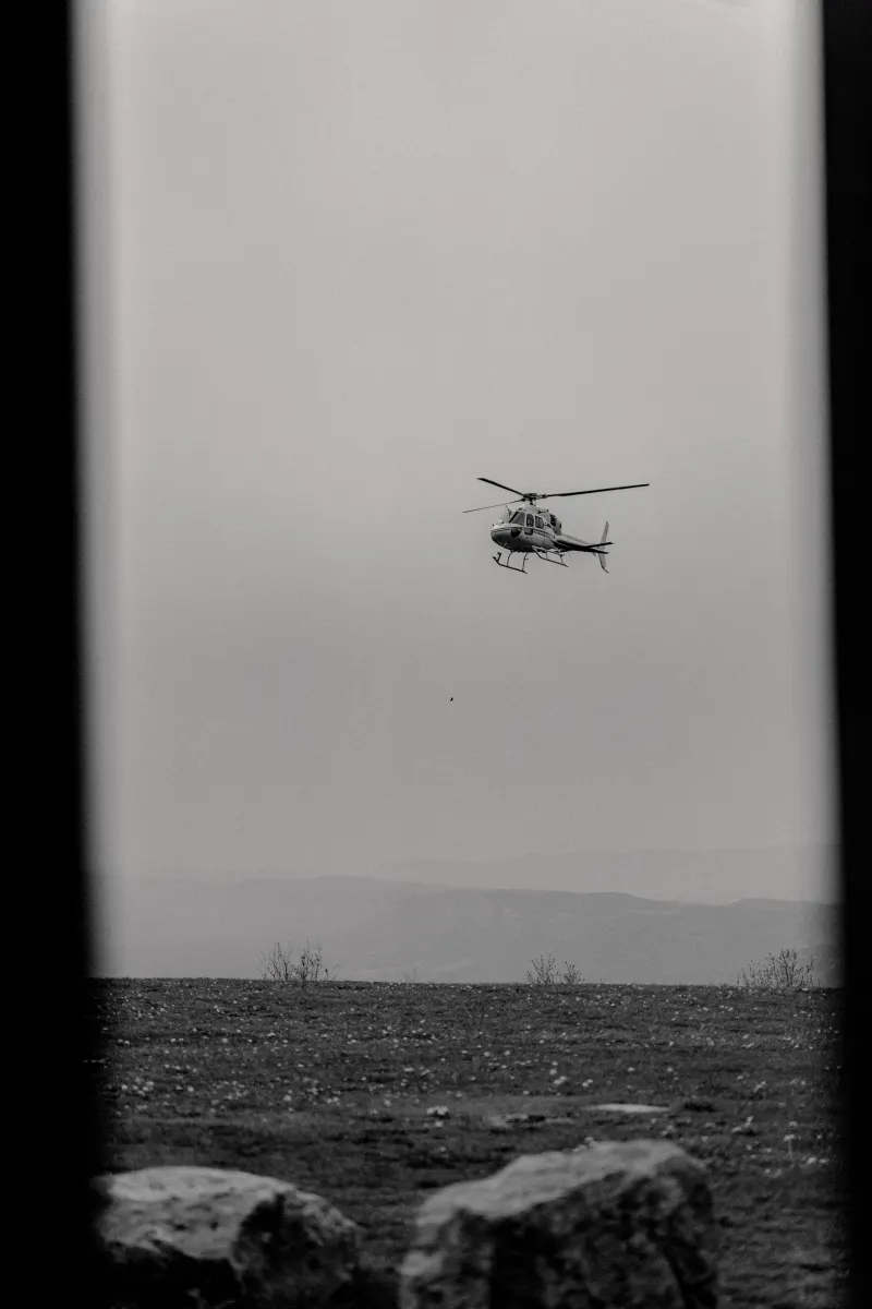 Helicopter approaches a scenic hilltop for a surprise proposal photoshoot, capturing anticipation in black and white.