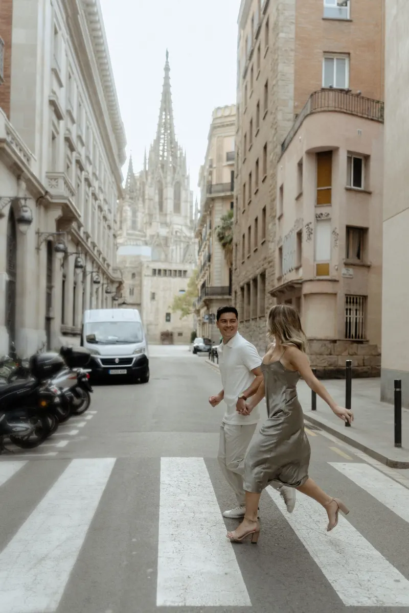 Joyful couple crossing a Barcelona street hand in hand during a Vacation Portraits session near the cathedral.