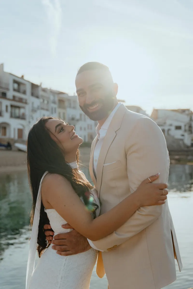 Joyful couple embraces by the water at sunset during a surprise proposal photoshoot in a charming coastal village.