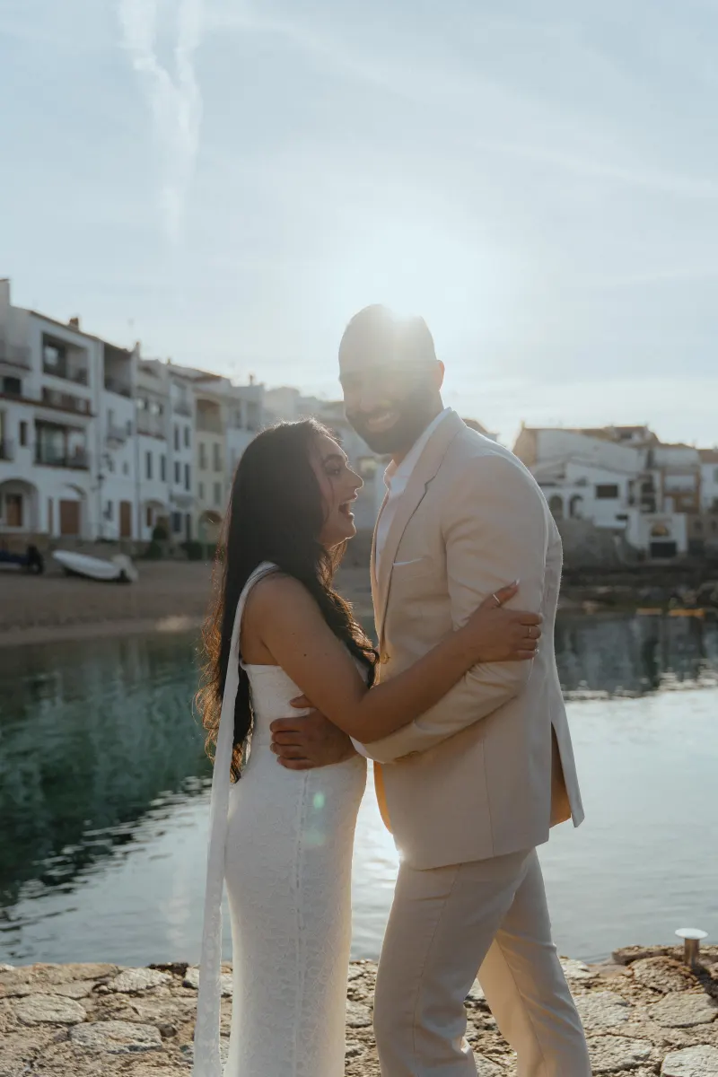 Joyful couple embraces by the waterfront at sunset during a surprise proposal photoshoot in a charming coastal town.