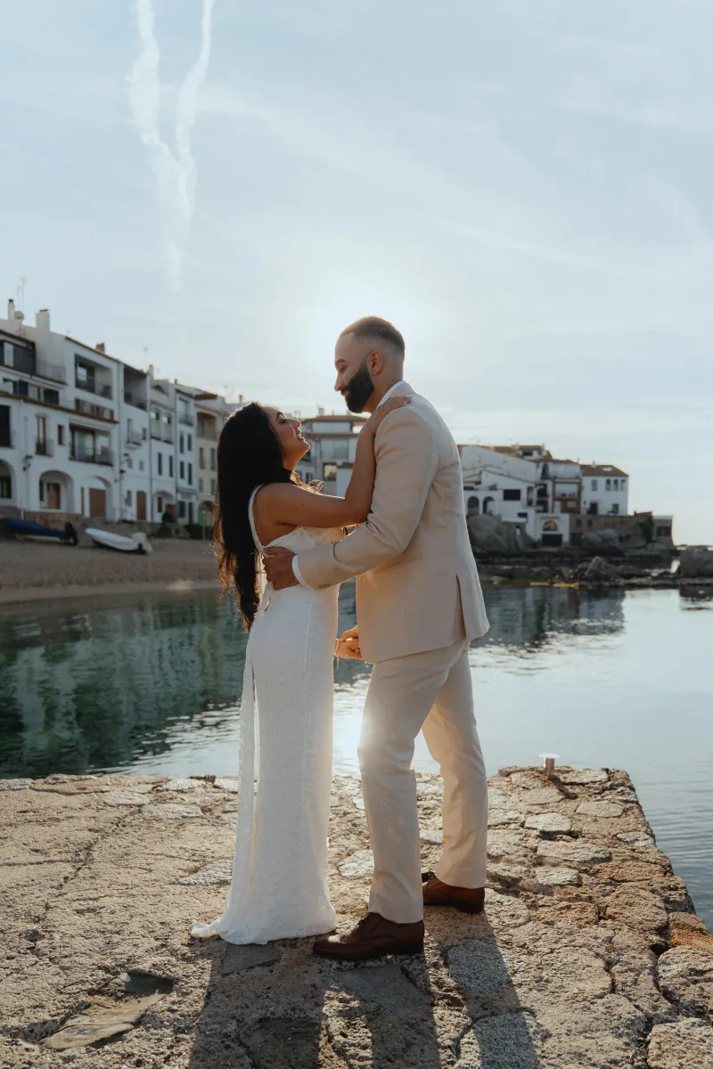 Joyful couple embraces by the waterfront at sunset during a surprise proposal photoshoot in a charming coastal village.