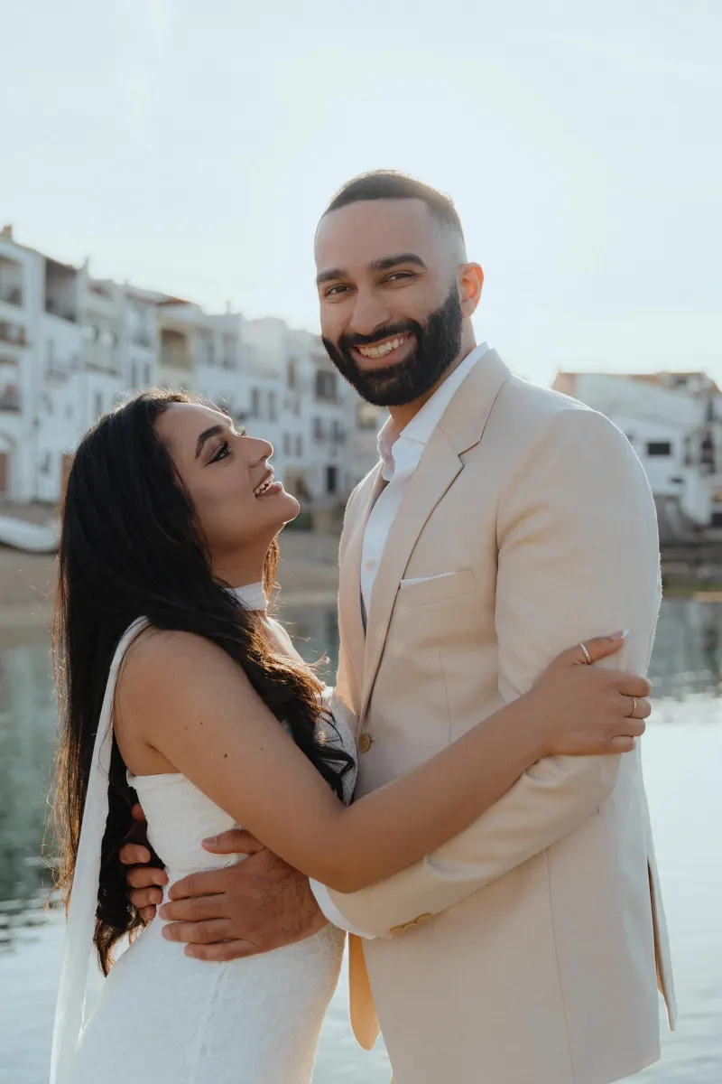 Joyful couple embraces by the waterfront during a surprise proposal photoshoot, sunlight and smiles all around.