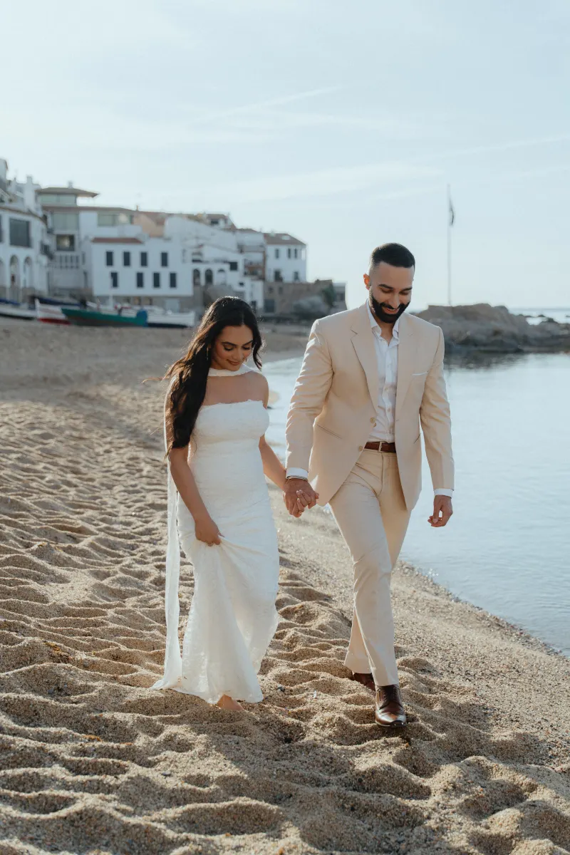 Joyful couple holding hands during a surprise proposal photoshoot, walking barefoot on a sunlit beach.