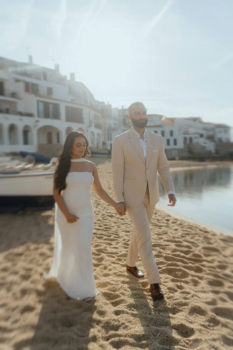Joyful couple holding hands on a sunlit beach, captured during a surprise proposal photoshoot in a coastal village.