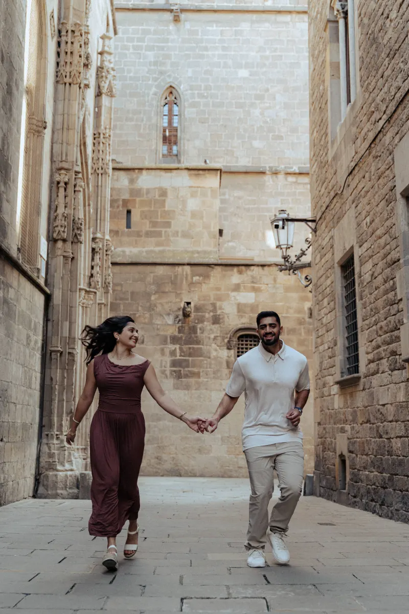 Joyful couple runs hand in hand through a sunlit historic alley during their couples & engagements photoshoot.