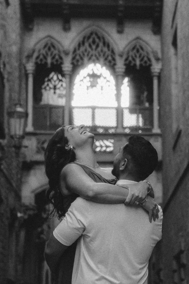 Joyful couple shares a carefree embrace beneath gothic arches during a couples & engagements photoshoot in the old city.