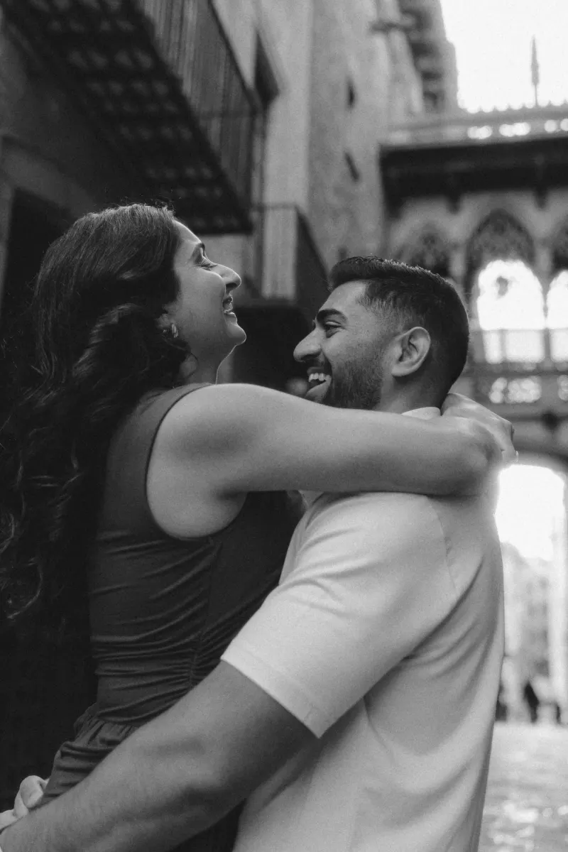 Joyful couple shares a close embrace and laughter during their couples & engagements photoshoot in a historic city alley.