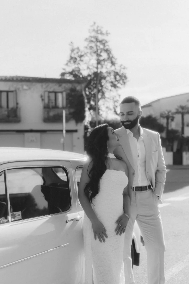 Joyful couple shares a loving gaze beside a classic car, captured during a surprise proposal photoshoot.