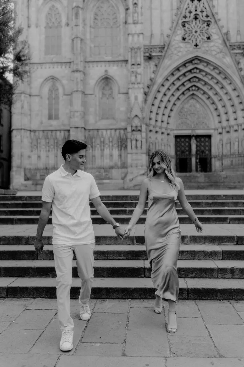 Laughing couple descending cathedral steps in Barcelona, captured during a Vacation Portraits photoshoot.