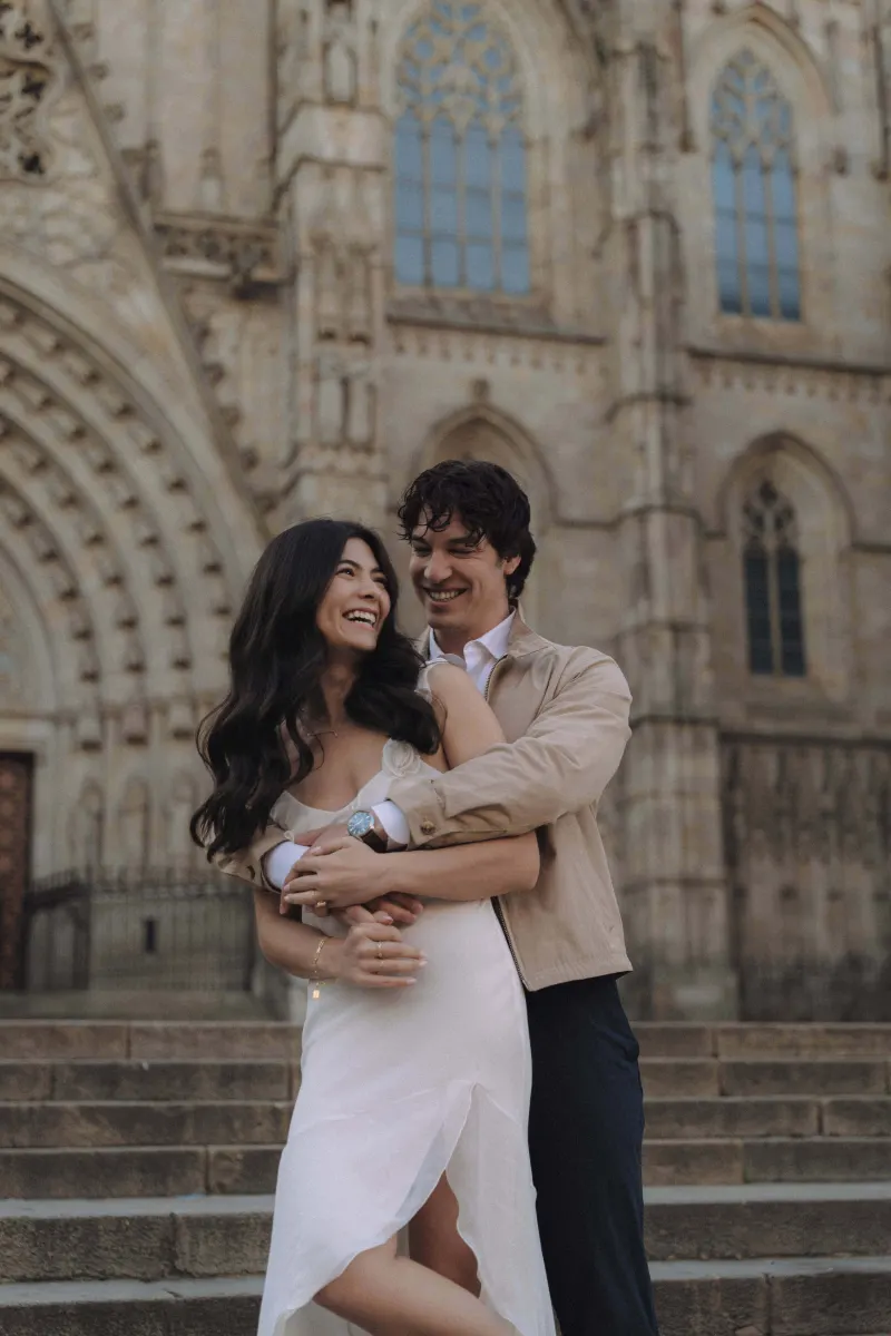 Laughing couple embraces on cathedral steps during a couples & engagements photoshoot, radiating joy and connection.